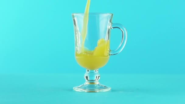 Slow motion close-up shot of fruit orange multifruit juice cold beverage drink pooring into latte glass mug blue background in studio — Stock Video