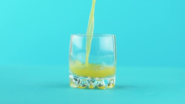 Meyve portakal multifruit suyu soğuk içecek içki pooring Studio küçük güzel cam mavi arka plan içine, ağır çekim yakın çekim vurdu — Stok video