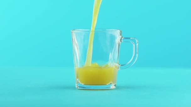 Slow motion close-up shot of fruit orange multifruit juice cold beverage drink pooring into glass mug with handle blue background in studio — Stock Video