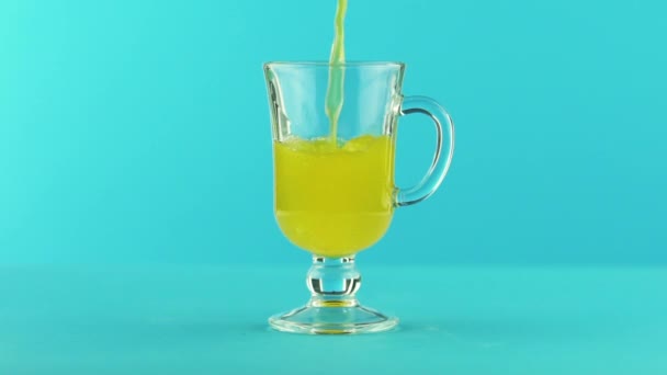 Slow motion close-up shot of fruit fizzy orange soda cold beverage pooring into latte glass mug blue background in studio — Vídeo de Stock