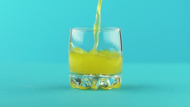 Slow motion close-up shot of fruit fizzy orange soda cold beverage drink pooring into small beautiful glass blue background in studio — Stock Video