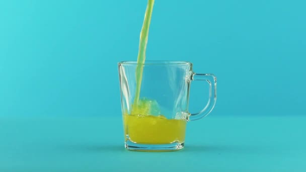 Slow motion close-up shot of fruit fizzy orange soda cold beverage drink pooring into glass mug with handle blue background in studio — Stock Video