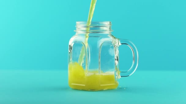 Slow motion close-up shot of fruit fizzy orange soda cold beverage drink pooring into glass jar mug blue background in studio — Stock Video