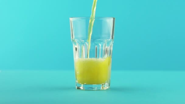 Медленное движение крупным планом снимок фруктового газированного напитка с апельсиновой газировкой, переходящего в граненое стекло на цветном голубом фоне в студии — стоковое видео
