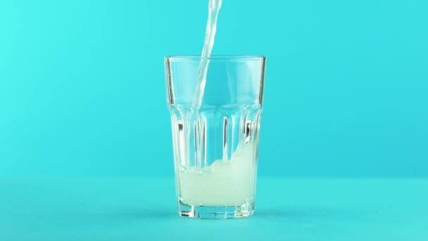 Plan rapproché au ralenti d'une boisson gazeuse à la limonade pétillante aux fruits dans un verre facetté sur fond bleu coloré en studio — Video
