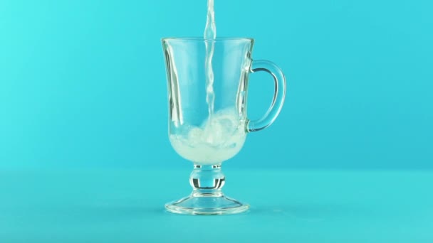 Slow motion close-up shot of fruit fizzy lemonade soda cold beverage drink pooring into latte glass mug blue background in studio — Stock Video