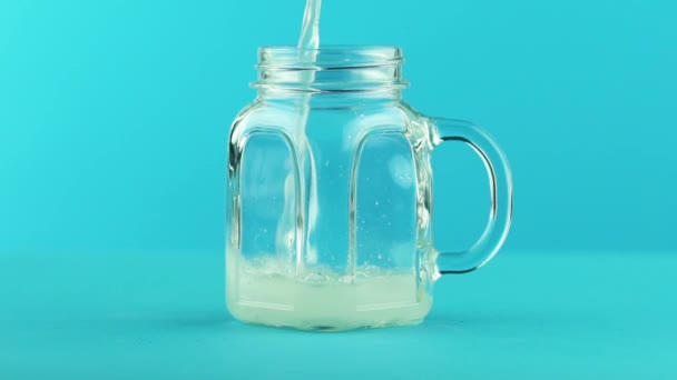 Plan rapproché au ralenti d'une boisson gazeuse à la limonade pétillante à base de fruits et de boissons froides dans une tasse en verre fond bleu en studio — Video