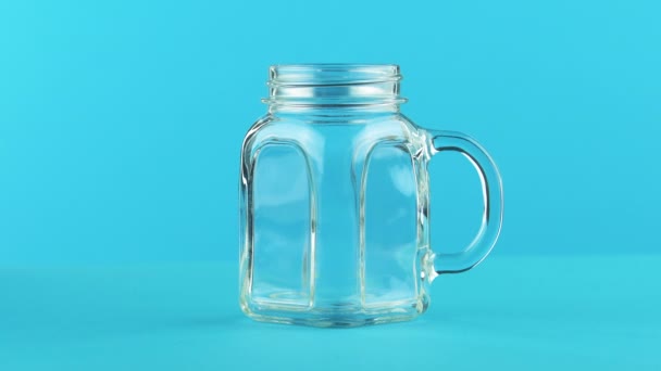 4K primer plano de la bebida fría de leche bebida pooring en jarra de vidrio taza fondo azul en el estudio — Vídeos de Stock