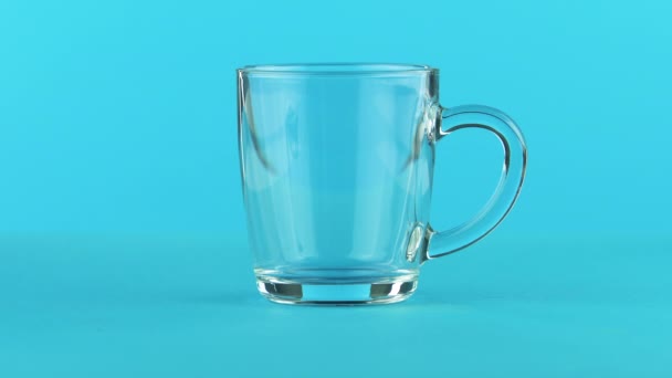 4K gros plan de boisson froide au lait dans une tasse en verre avec poignée arrondie fond bleu en studio — Video