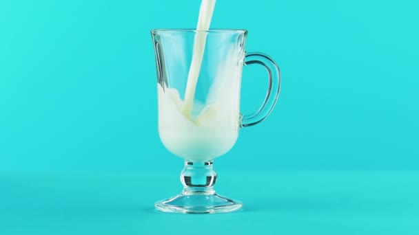 4K крупным планом снимок холодного молочного напитка, переливающегося в стакан латте, голубой фон в студии — стоковое видео