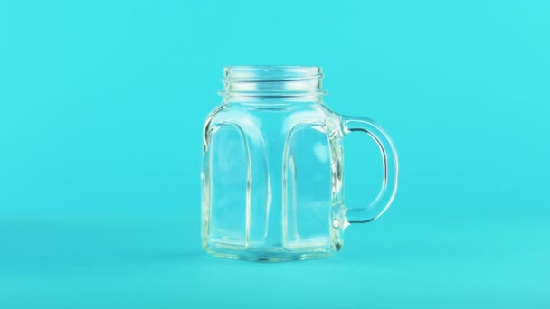 4K primer plano de fruta jugo multifruta bebida fría bebida pooring en jarra de vidrio taza fondo azul en estudio — Vídeos de Stock