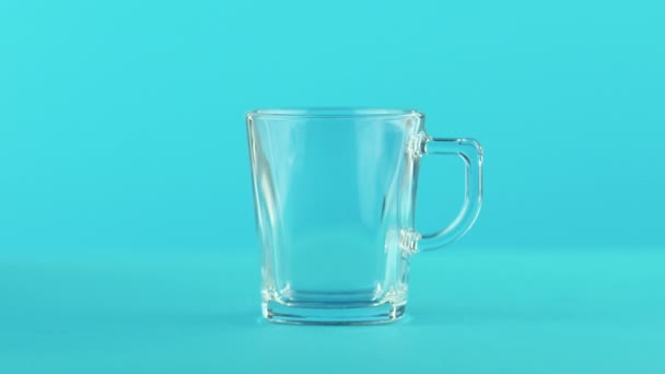 4K plan rapproché de fruits orange pétillante boisson froide braconnage dans une tasse en verre avec poignée fond bleu en studio — Video