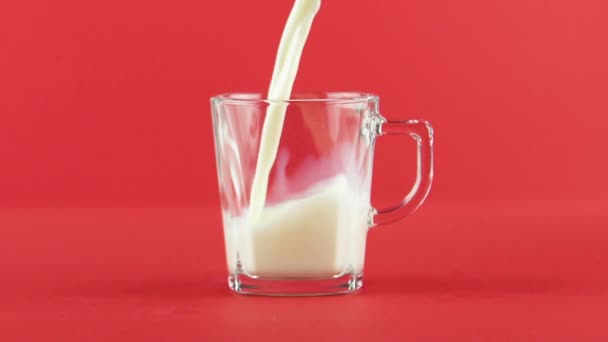 Slow motion close-up shot of cold diary milk cold beverage drink pooring into glass cup with facets red background in studio — Stock Video