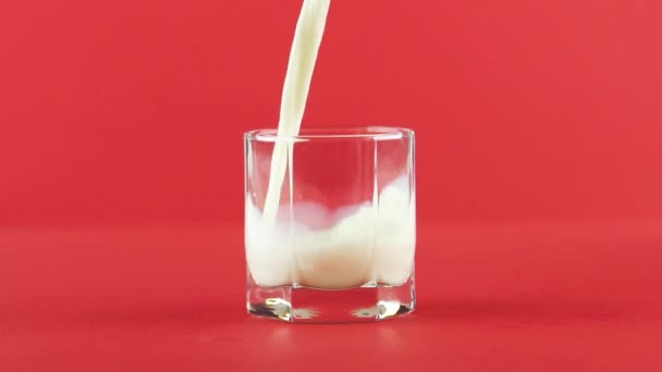 Slow motion close-up shot of cold diary milk cold beverage pooring into low glass with facets red background in studio — Vídeo de Stock