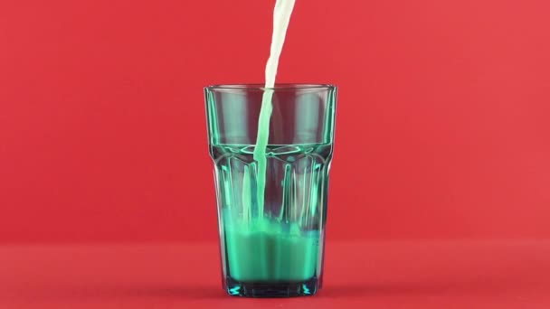 Slow motion close-up shot of cold diary milk cold beverage drink pooring into blue faceted glass red background in studio — Stock Video