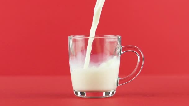 Lambat gerak close-up shot of cold diary milk cold drink pooring into glass mug with rounded handle red background in studio — Stok Video