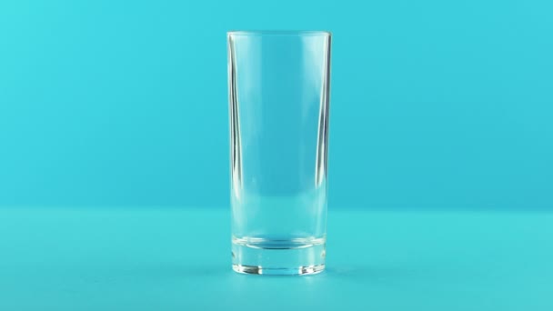 4 k close-up shot van gele citroen koolzuurhoudende limonade frisdrank koud drankje drinken massasprint in naar lage glas blauwe achtergrond in de studio — Stockvideo