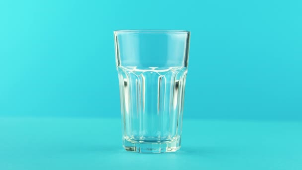 4K close-up shot of yellow lemon fizzy lemonade soda cold beverage drink pooring into faceted glass on colored blue background in studio — Stock Video