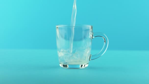 4K close-up shot of yellow lemon fizzy lemonade soda cold beverage drink pooring into glass mug with rounded handle blue background in studio — Stock Video