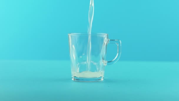 4K gros plan de citron jaune fizzy limonade soda boisson froide pooring dans une tasse en verre avec poignée fond bleu en studio — Video