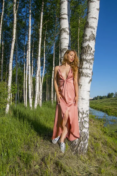 Joven esbelta hermosa chica en un vestido de coral largo posando en un bosque de abedules sonriendo en verano día de verano — Foto de Stock