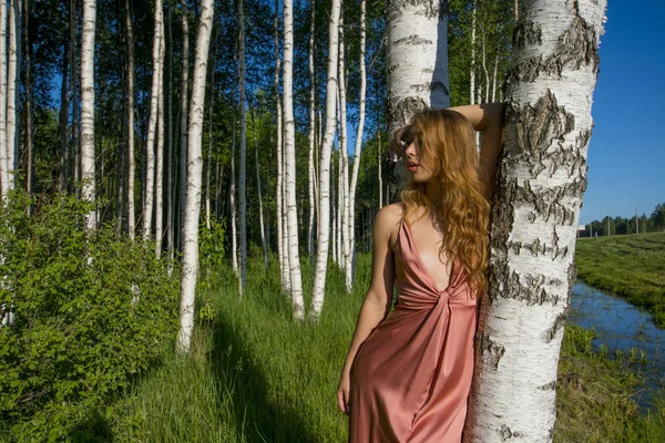 vogue çözüm kafasına el ile gülümseyen bir huş ağacı koru poz uzun mercan elbiseli Genç ince güzel kız