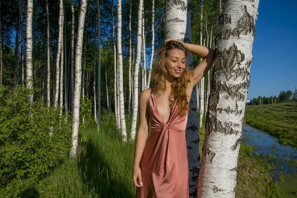 Feliz joven esbelta hermosa chica en un vestido de coral largo posando en un bosque de abedules sonriendo — Foto de Stock