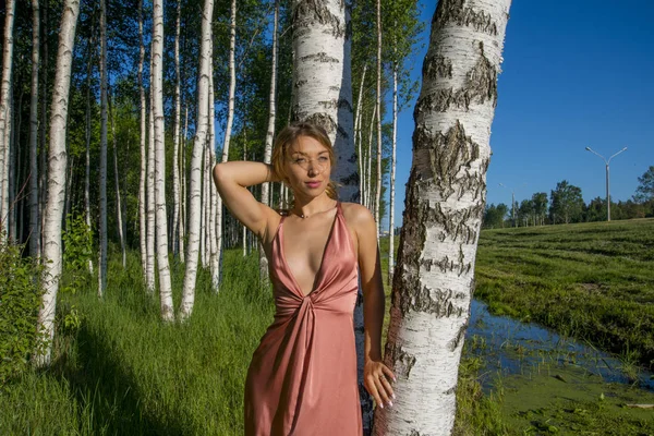 Genç ince uzun bir mercan kız güzel elbise ile onun çıplak göğüs gülümseyen bir huş ağacı koru poz