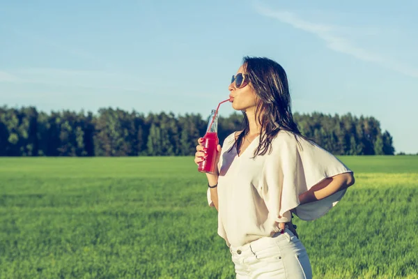 youn ince kız gözlük ve kıvırcık saç gülümseme ve bir alkollü veya alkolsüz kırmızı kokteyl kamışla bir güneşli yaz gün gülümseyerek üzerinde bir şişe içki