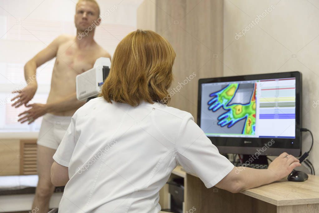 a young man at a doctors reception on a thermographic study with a thermal imager examining the limbs of his hands