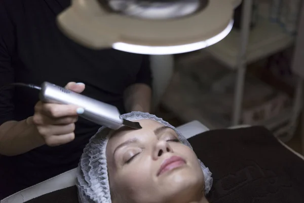 Primo piano ritratto di bella donna e mano con dispositivo di sollevamento cosmetico toccare il suo viso sotto la lampada — Foto Stock