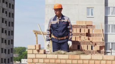 Minsk, Beyaz Rusya, 14 Ağustos 2018 - Builder tuğladan bir apartman inşa ediyor. İşçi bir şantiyeye tuğla döşer. Tuğla sanayi