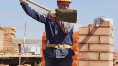 Minsk, Beyaz Rusya, 14 Ağustos 2018 - İnşaatçılar kırmızı tuğladan bir apartman inşa ediyorlar. İşçi bir şantiyeye tuğla döşer. Tuğla sanayi