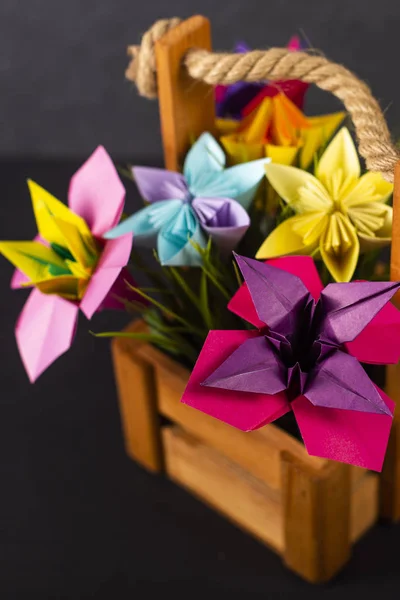 Handmade colored paper flowers origami bouquet paper craft art in a basket with grass in the studio on colored background closeup macro