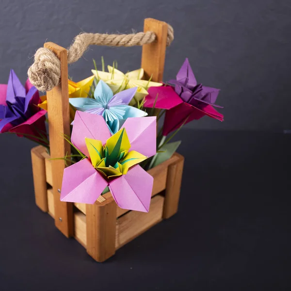 Handmade colored paper flowers origami bouquet paper craft art in a basket with grass in the studio on colored background macro