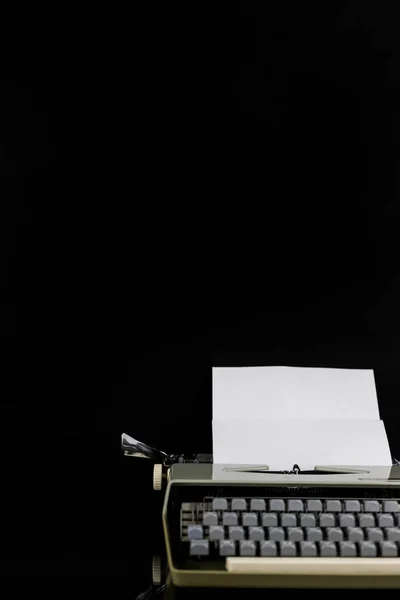 Psací stroj na černém pozadí s bílým papírem s prázdným prostorem. Pracovní plocha spisovatele nebo autora. Koncepce idejí. — Stock fotografie