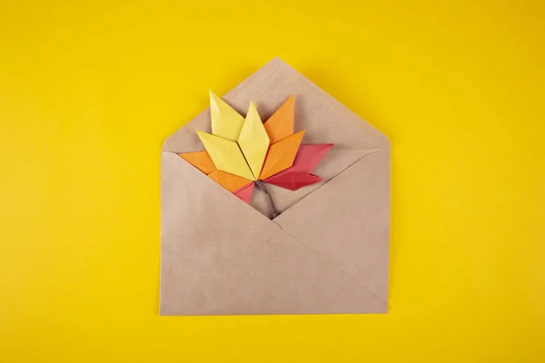 Origami papercraft autumn concept fallen leaves letter in an envelope on a yellow background handmade craft art