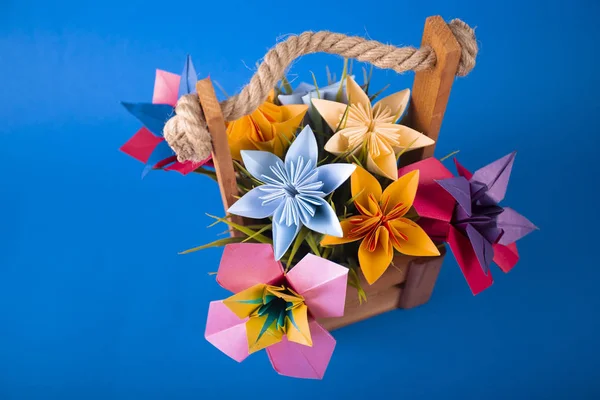 Flores de papel de colores hechos a mano origami ramo de papel arte artesanal en una cesta con hierba en el estudio sobre fondo azul de color — Foto de Stock