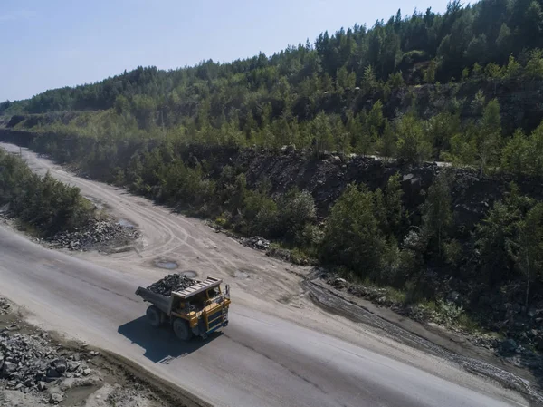 Huge industrial dump truck in a stone quarry loaded transporting marble or granite shot from a drone in nature