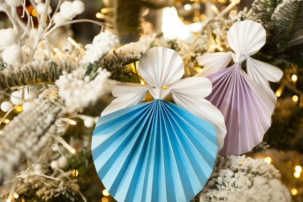 Новогодние фигурки ручной работы ангела-оригами на рождественской елке с праздничными украшениями с теплыми огнями. Концепция зимних открыток студия крупным планом — стоковое фото