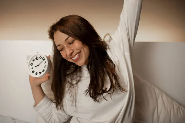 Linda chica caucásica con el pelo oscuro se despierta de un reloj despertador y se extiende — Foto de Stock