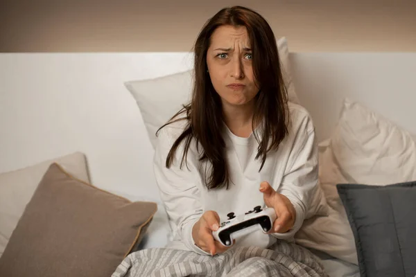 Jolie fille aux cheveux foncés dans la chambre à coucher joue à des jeux vidéo sur console en utilisant une manette de jeu — Photo