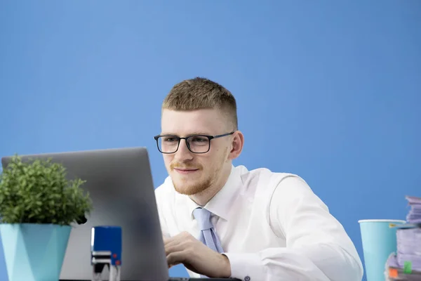 Joven trabajador de oficina sonriente trabaja entusiasta e intensamente en un ordenador portátil — Foto de Stock