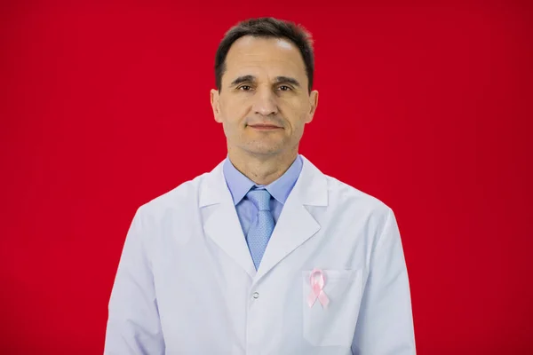 Lächelnder Arzt in weißem Mantel mit rosa Schleife auf rotem Hintergrund — Stockfoto