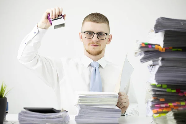 Trabajador de oficina en camisa, corbata y gafas sellos en pila de documentos sin terminar —  Fotos de Stock
