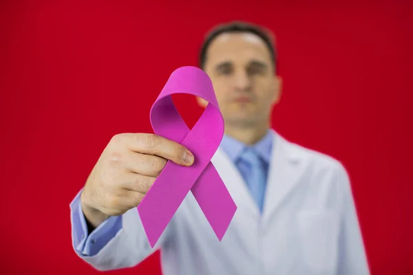 Close up pink ribbon in doctors hand on red background Breast cancer awareness — Stock Photo, Image