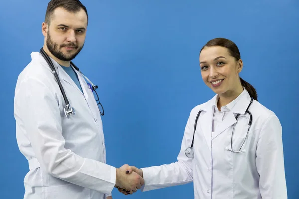 Zwei attraktive Ärzte beim Händeschütteln auf blauem Hintergrund, Deal, Kollaboration — Stockfoto