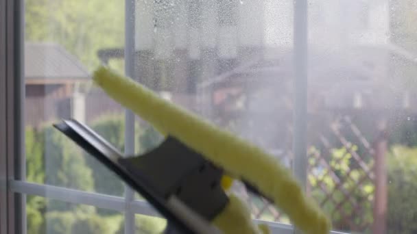 Νοικοκυρά ψεκάζει το απορρυπαντικό στο παράθυρο και σκουπίζει το παράθυρο με ύφασμα μικροϊνών — Αρχείο Βίντεο