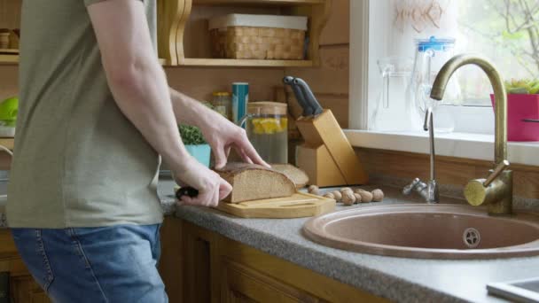 Blanc beau homme coupe le pain en morceaux avec un couteau de cuisine tranchant sur une planche en bois de chêne. — Video