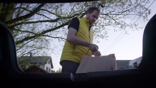 Muž dává nákupní tašky do kufru auta. Nakládání do zavazadlového prostoru — Stock video